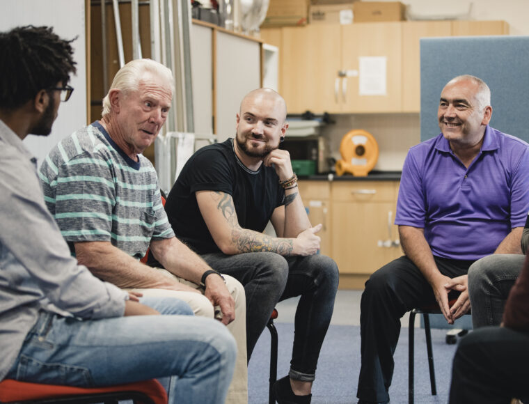 Group of men are talking and laughing together in a mental health support group.