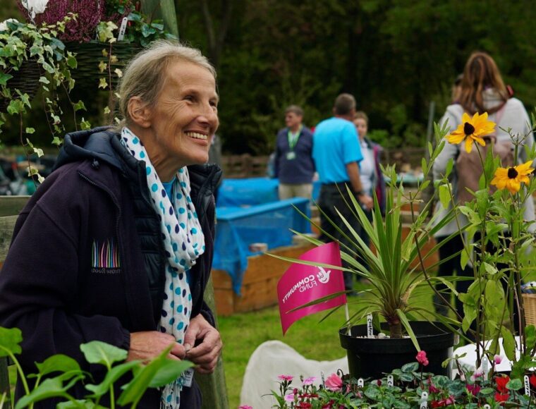 Gardening project volunteer poses in front of a plant stall duing an open day event at Roots Luton