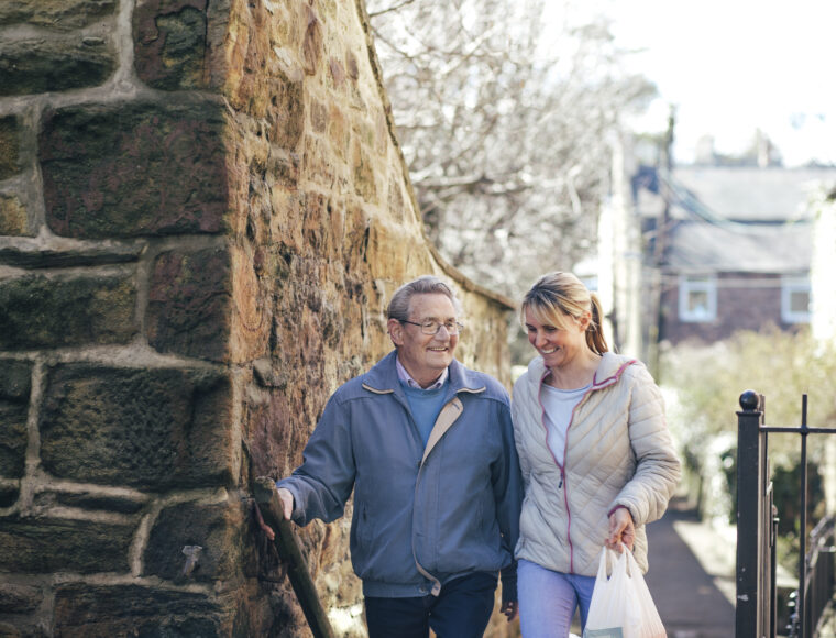 A man walks home from grocery shopping with a support worker.
