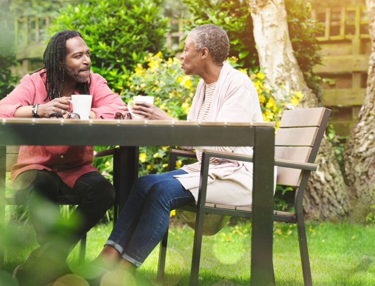 Two adults enjoying a coffee while siting together in a garden outside.